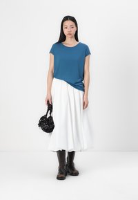 Un top teal cu mânecă scurtă, asortat cu o fustă albă voluminoasă, purtat cu cizme maro până la genunchi și o geantă neagră cu modele florale.