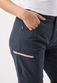 Ciemnoszare spodnie z różową kieszenią na zamek błyskawiczny i małym akcentem w postaci szwedzkiej flagi w pobliżu pasa. Tkanina wygląda na gładką i elastyczną.