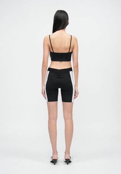 Černý crop top s tenkými ramínky, spárovaný s černými šortkami s bílými bočními panely. Hladký materiál, přiléhavý střih, ukazující zadní pohled.