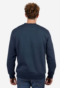 Sudadera azul marino con cuello redondo, hecha de tela suave, con puños y dobladillo acanalados, textura lisa y sin patrones visuales.