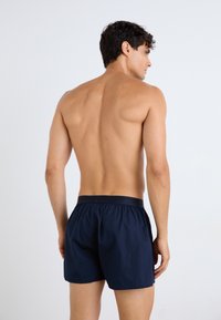 Mørkeblå badshorts med elastisk liv, laget av lett materiale, med et enkelt design uten mønstre eller detaljer.