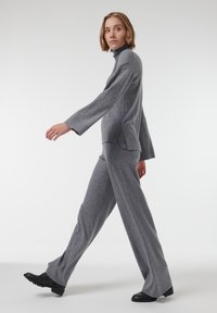 Grijze gebreide trui met een hoge kraag en splitzoom, gecombineerd met bijpassende grijze wijde broeken. Voorzien van lange mouwen en stijlvolle zwarte schoenen.