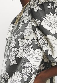 Kwiatowa bluzka w czerni i bieli, charakteryzująca się luźnym krojem, dużymi rękawami oraz teksturowanym materiałem z wyraźnymi wzorami kwiatowymi.