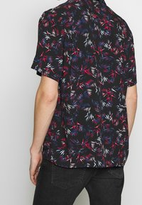 Kurzarmhemd aus schwarzem Stoff mit buntem Blattmuster in Rot, Blau und Weiß. Das Design umfasst einen geraden Saum und eine lockere Passform.
