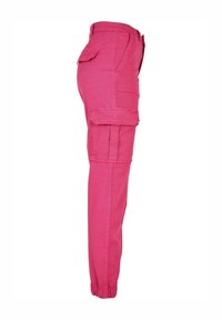 Pantalon cargo rose avec poignets élastiques, poches latérales à rabat et une taille haute, présenté de profil sur fond blanc.