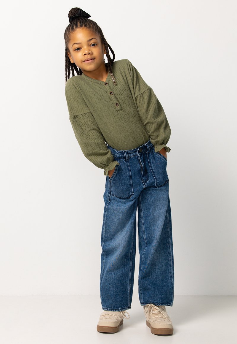 Groene wafelweave button-up top met lange mouwen, gecombineerd met hooggetailleerde, wijdvallende blauwe spijkerbroek. Beige schoeisel maakt de outfit af.