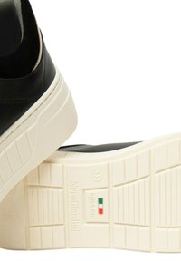 Sneaker in pelle nera con suola in gomma bianca. Presenta dettagli testurizzati e il marchio "Nero Giardini" sulla suola. Prodotto in Italia.