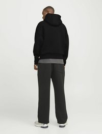 Felpa nera con cappuccio e vestibilità ampia, abbinata a pantaloni grigi scuri a gamba larga. Presenta una tasca sul retro e sneaker bianche.