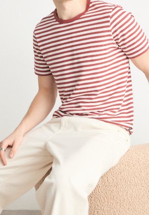 Rot-weiß gestreiftes T-Shirt mit kurzen Ärmeln und rundem Ausschnitt, kombiniert mit hellbeigen Hosen. Strukturierte Oberfläche und lockere Passform.