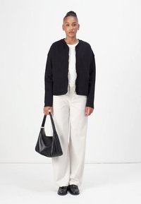 Schwarze verkürzte Jacke mit rundem Ausschnitt und goldenen Beschlägen, kombiniert mit weißen weiten Hosen und einer schwarzen Lederhandtasche. Glatte Texturen.