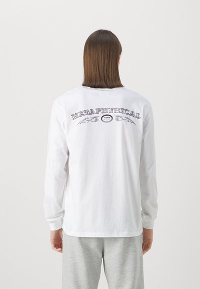 Long-sleeve white t-shirt featuring a back graphic that reads “METAPHYSICAL” in bold stylized font, with decorative accents and a curved line design.