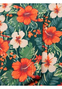 Květinová látka s velkými oranžovými hibisky a bílými květinami na zeleném listovém pozadí. Materiál se zdá být lehký a má hladkou texturu.