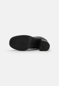 Semelle de chaussure habillée noire avec des motifs de grip texturés, vue de dessous sur fond blanc, mettant en avant le design de la bande de roulement et du talon.