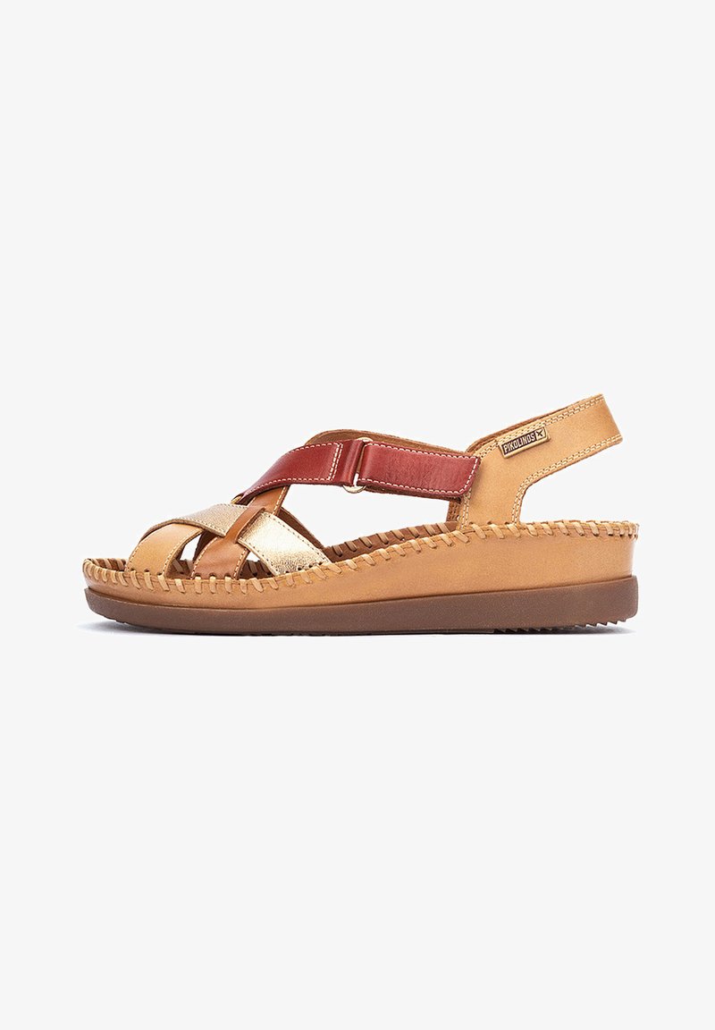 Sandal en cuir tan avec un design entrecroisé et des accents dorés et rouges. Présente une semelle épaisse et un bord cousu pour plus de texture. Sangle ajustable.