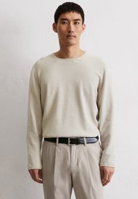 Beige gebreide trui met lange mouwen en een textuurafwerking, gecombineerd met beige broek en een zwart leren riem met een zilveren gesp.