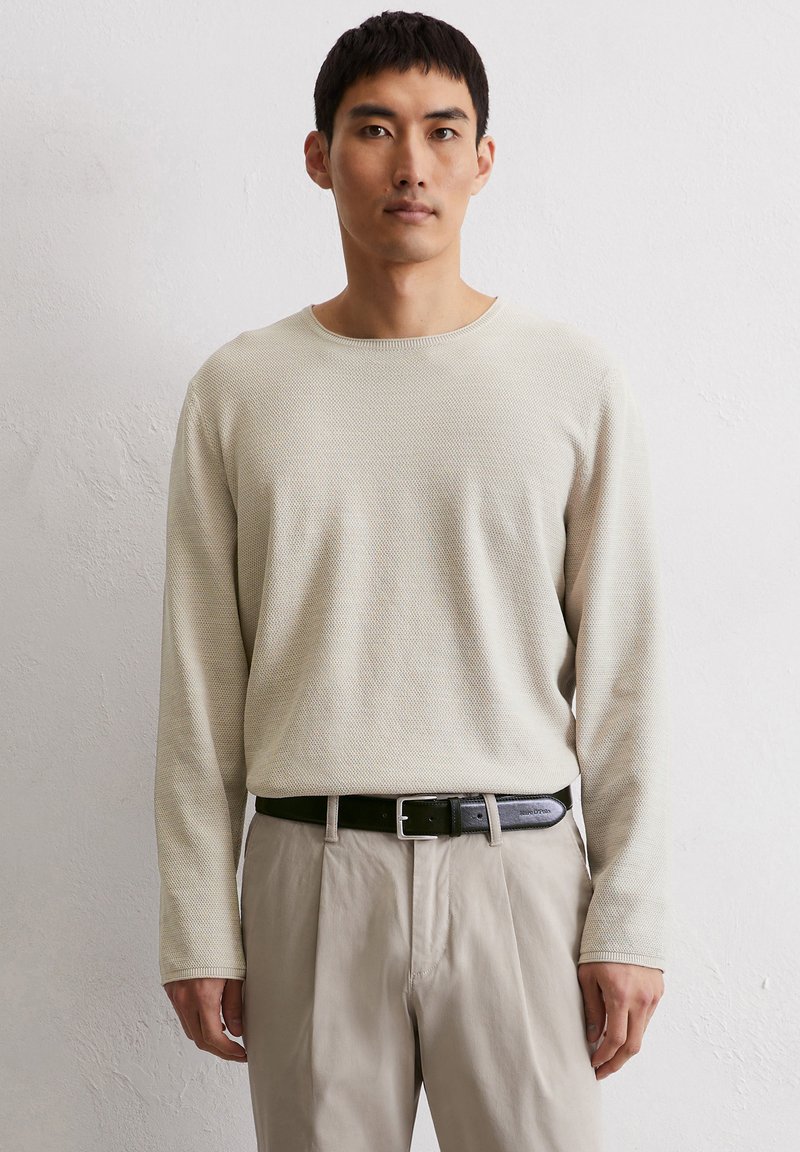 Beige gebreide trui met lange mouwen en een textuurafwerking, gecombineerd met beige broek en een zwart leren riem met een zilveren gesp.