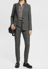 Blazer à carreaux gris et pantalon assorti, avec une chemise gris clair. Tissu lisse, design ajusté et mocassins noirs en cuir verni.