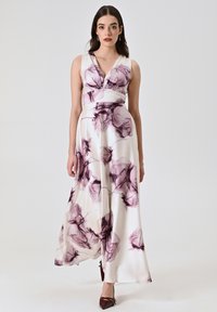 Robe longue blanche avec imprimé floral violet, décolleté en V, corsage ajusté et jupe fluide. Fabriquée en tissu lisse, elle possède une fente latérale.