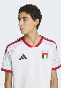 Maillot de football blanc avec accents rouges, présentant une manche à motif géométrique, logo Adidas et emblème de la FA des Émirats arabes unis sur la poitrine.
