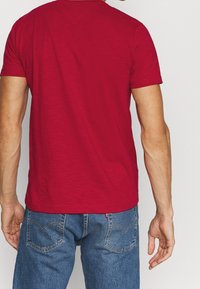 Maglietta rossa a maniche corte realizzata in tessuto morbido, con collo rotondo e design semplice. Il retro presenta una superficie liscia e priva di decorazioni.