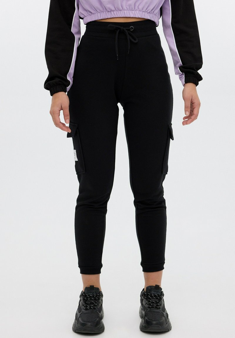 Pantalones de chándal cargo negros hechos de un tejido suave, con piernas ajustadas, bolsillos laterales y cintura con cordón para un ajuste ajustable.