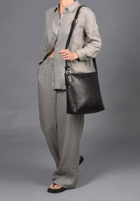 Bolso tote de cuero negro con correa ajustable, forma rectangular, textura suave, combinado con una blusa de lino gris claro y pantalones holgados.