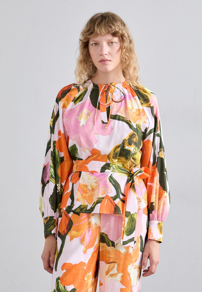 Blusa floreale in rosa, arancione e verde, con scollatura arricciata, maniche lunghe e vita legata per una vestibilità regolabile.