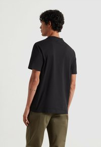 Czarna koszulka z krótkim rękawem, okrągłym dekoltem, gładką teksturą, luźnym krojem i równym dołem, zestawiona z jasnymi oliwkowymi spodniami.