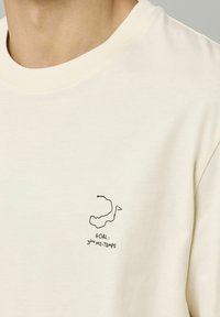 T-shirt couleur crème avec un dessin à ligne noire et le texte "OBJECTIF : 3ème MI-TEMPS." Matière douce avec un design classique à col rond.