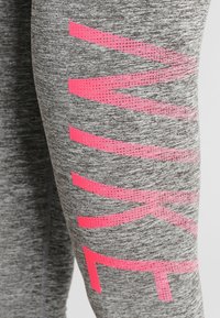 Leggings grigi con un grande logo "NIKE" rosa in un design grafico audace, caratterizzato da un motivo testurizzato. Il tessuto sembra morbido e elastico.
