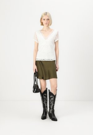 Koronkowa biała bluzka z krótkim rękawem, oliwkowa spódnica, czarne kowbojskie buty z srebrnym haftem oraz mała czarna torebka.