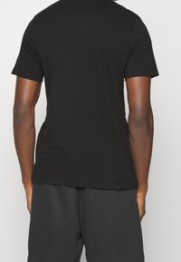 Czarny t-shirt z krótkim rękawem wykonany z miękkiej bawełny, z okrągłym dekoltem i luźnym krojem. Gładka faktura z przeszytymi szwami.