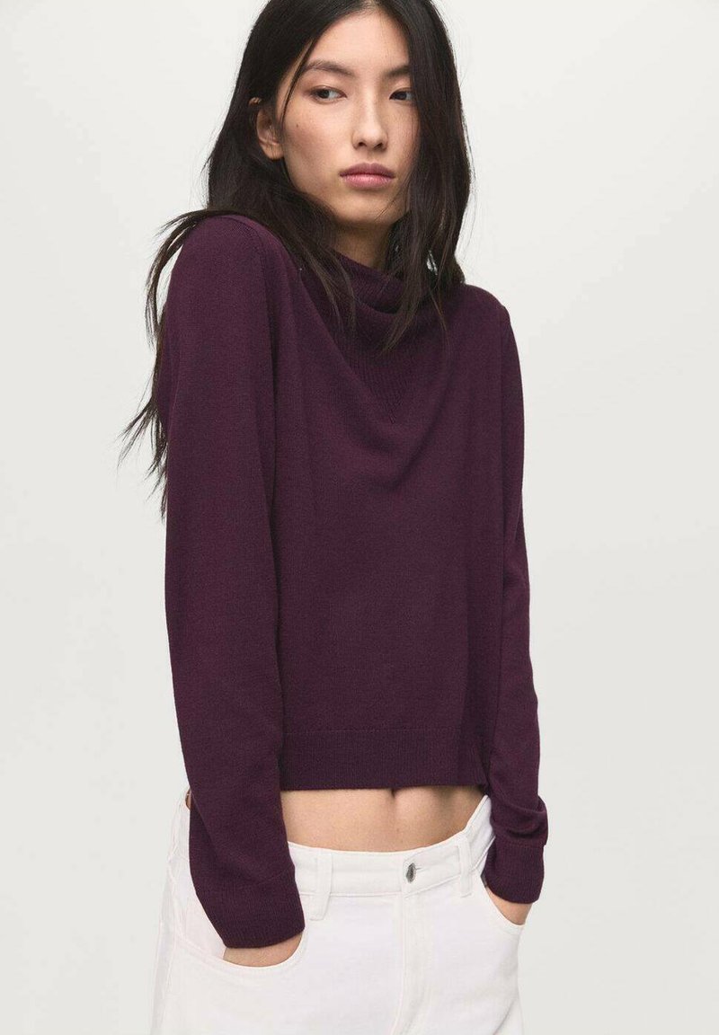 Suéter corto de manga larga en punto morado profundo, con cuello vuelto y textura suave, combinado con pantalones blancos de cintura alta.