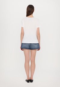 White short-sleeve t-shirt viewed from the back, made of soft fabric. Paired with blue denim shorts featuring two back pockets.