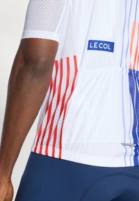 White cycling jersey with mesh panels. Features red and blue vertical stripes; “LE COL” logo on a blue tag. Smooth texture, athletic fit.
