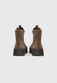 Bottines en suède marron avec une semelle noire épaisse, des zips latéraux et des détails de couture contrastés. La vue arrière met en avant la texture et le design.