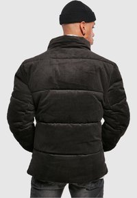 Chaqueta de puffer de pana negra con cuello alto y diseño acolchado, que presenta una superficie ligeramente texturizada y detalles de costura visibles.