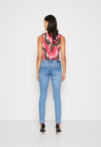 Sleeveless top with pink and green palm leaf pattern, paired with light blue skinny jeans and black high-heeled shoes.