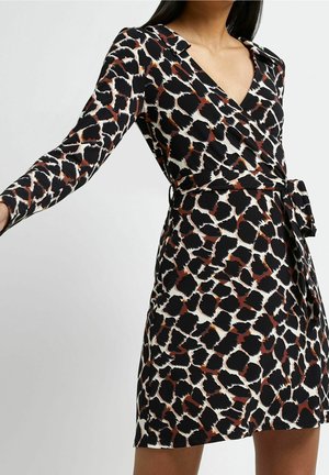 Frau trägt ein langärmeliges, V-Ausschnitt Wickelkleid mit abstraktem Tiermuster in Schwarz, Braun und Weiß sowie einem Seitenschleifen-Gürtel.