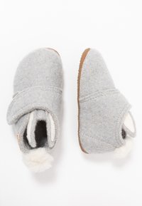 Sive papuče s zaobljenim vrhom, podesivim preklopom i smeškim gumiranim đonom. Imaju mekani beli pompon detalj na leđima.