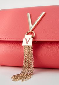 Koralli vaaleanpunainen kynä laukku, jossa on teksturoitu pinta, kultaketju tupsu ja voimakas metallinen "V"-koriste.