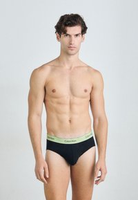 Boxeri negri din bumbac cu un tiv verde Calvin Klein, având un design ajustat și o textură netedă, purtați de un model cu o constituție atletică.