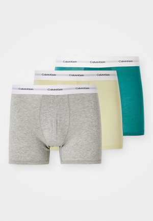 Três pares de boxers masculinos: cinza, amarelo e teal. Material em algodão com cós branco contrastante apresentando o logótipo "Calvin Klein".