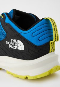 Baskets noires et bleues avec des accents jaunes, dotées d'un dessus texturé, d'un col rembourré et d'un logo proéminent. Semelle légère avec un motif de grip.