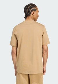 Tan katoenen t-shirt met korte mouwen, ontspannen pasvorm en een ronde hals. Het oppervlak heeft een gladde textuur zonder zichtbare patronen.