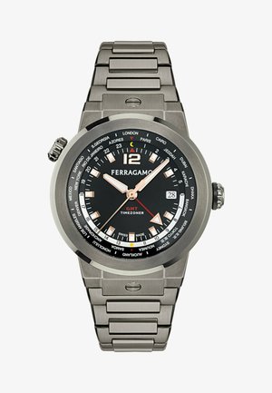 Ferragamo GMT sat s crnim brojčanikom, kućištem od nehrđajućeg čelika srebrne boje i narukvicom na spojnicama. Ima svjetlucave kazaljke i nazive gradova oko kućišta.
