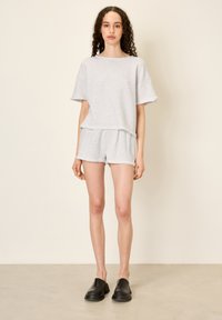 Pilkas medvilninis marškinėliai trumpomis rankovėmis ir atitinkantys šortai, pasižymintys laisvu kirpimu ir žaliais kraštais. Juodi šlepetės užbaigia aprangą.