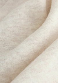 Ljusbeige stickad tyg med en mjuk, texturerad yta, som har subtila färgfläckar för en naturlig look.