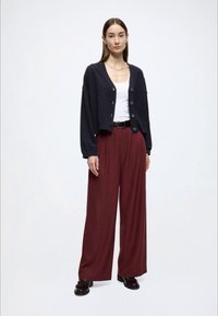 Granatowy krótki kardigan na guziki, biały top na ramiączkach, wysokie bordowe szerokie spodnie oraz czarne mokasyny. Prosty, dopasowany fason.