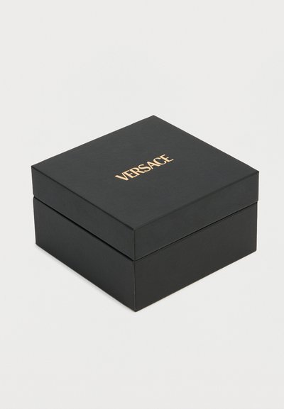 Boîte à bijoux carrée noire avec logo doré Versace centré sur le couvercle, sur fond blanc uni.